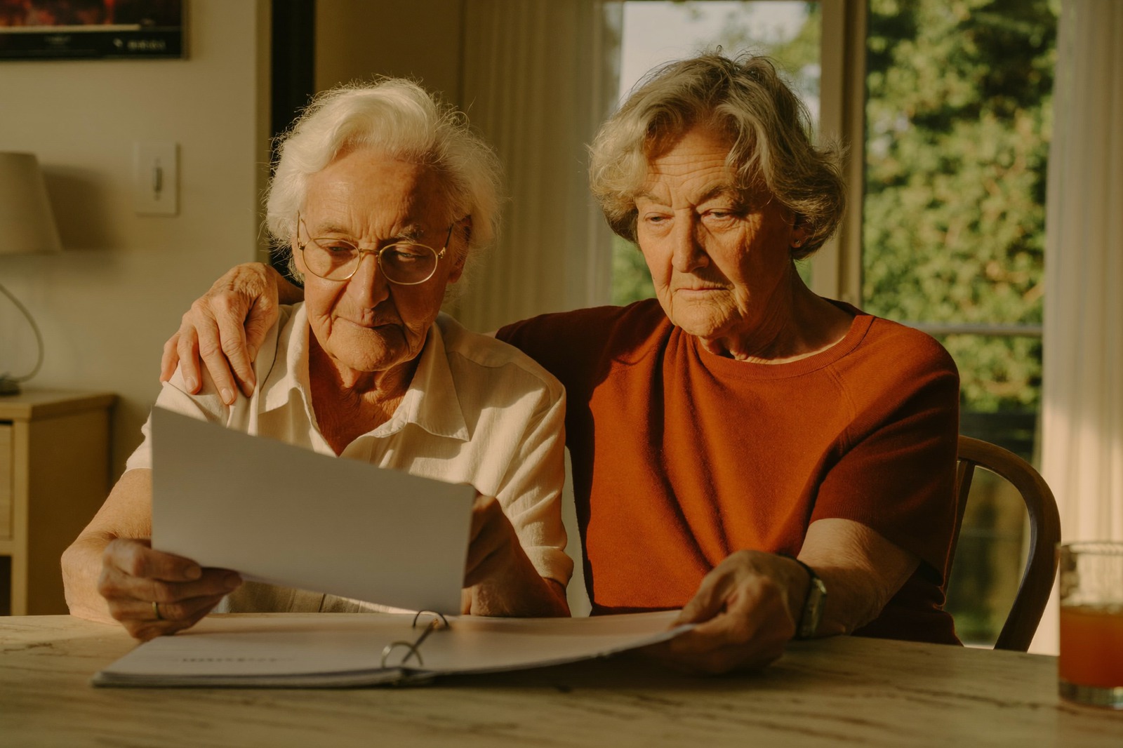 Two older women go through papers in a binder together at their kitchen table
