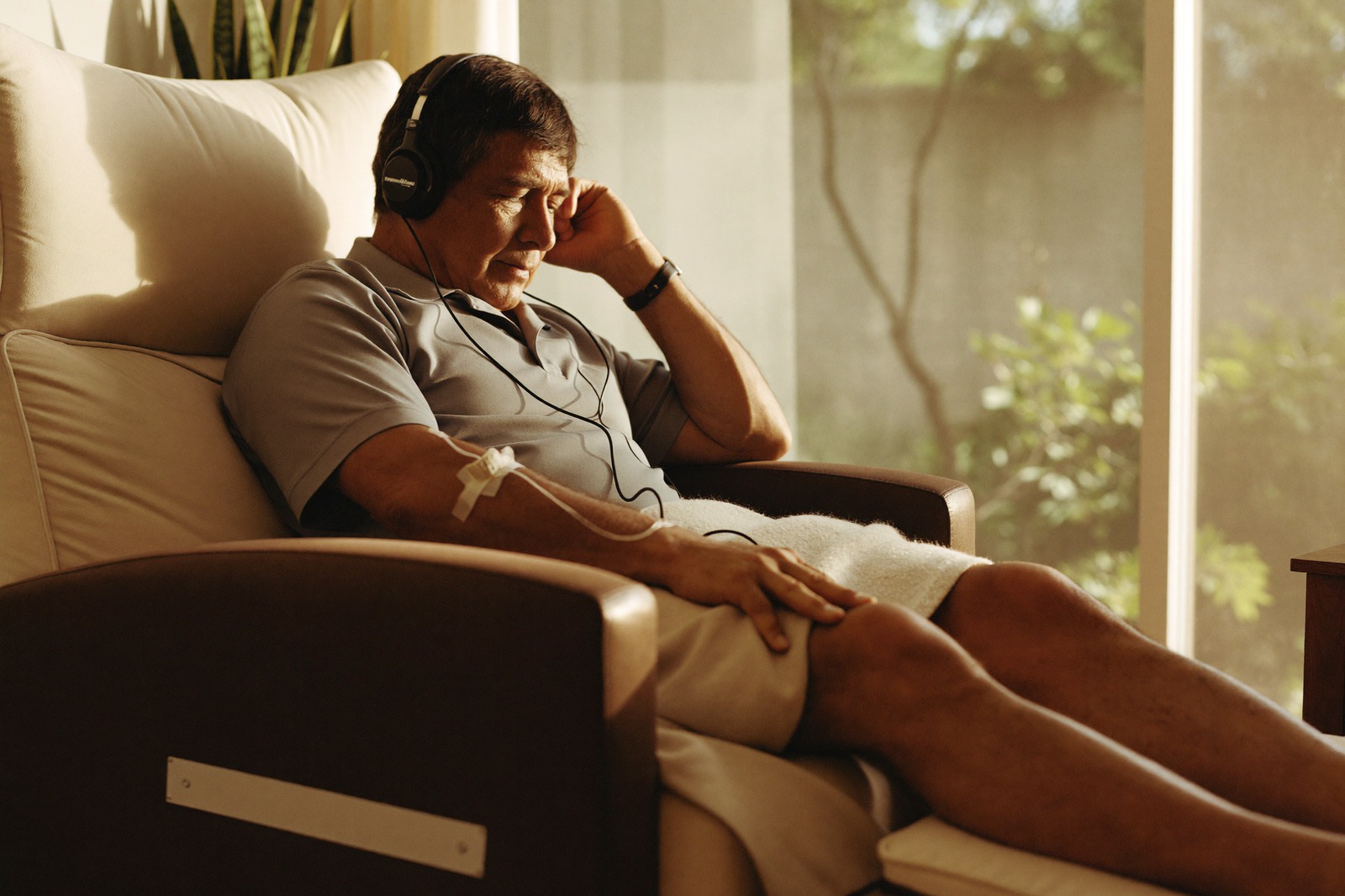 A man relaxes in an infusion recliner by a sunny window, listening to music on headphones