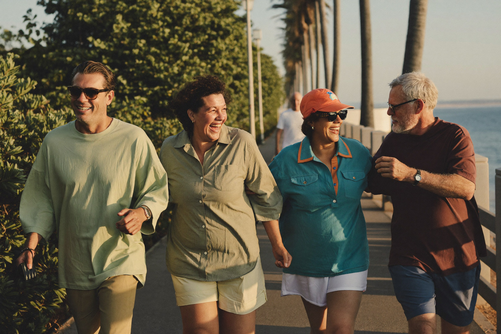 Four friends laugh as they walk together along a palm-lined Florida waterfront path