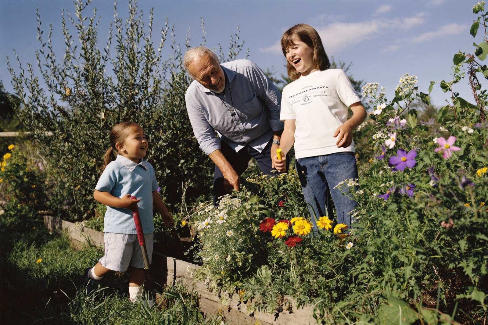A grandfather laughs while gardening with his two grandchildren