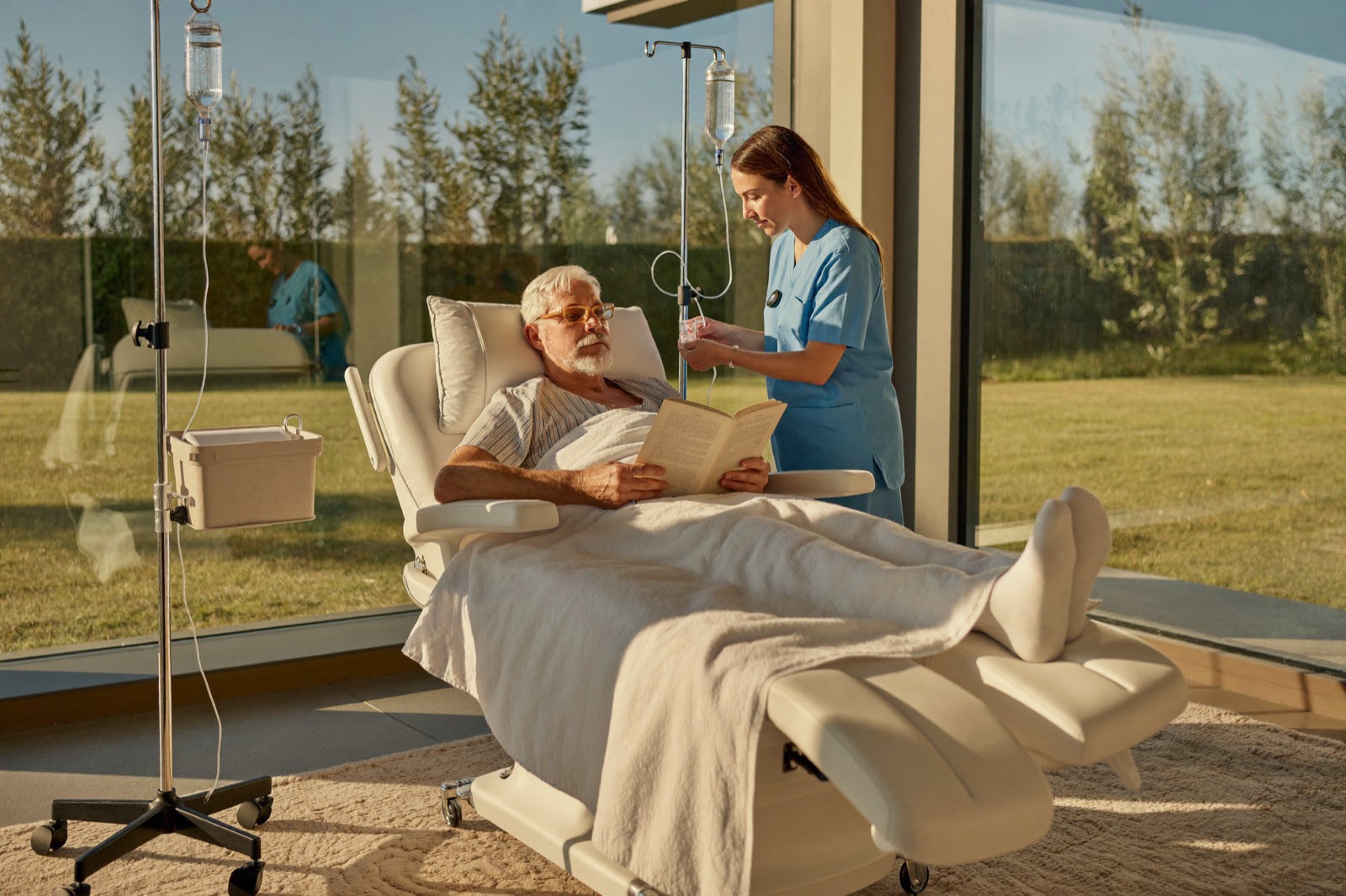 A patient relaxes in a bright infusion suite while a nurse adjusts an IV